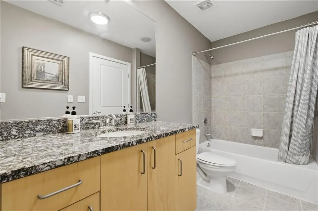 Bathroom featuring a single vanity with stone-finish countertop, light wood-finish cabinetry, and an undermount sink