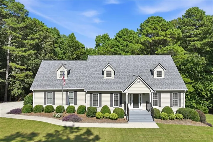 Light-toned siding exterior with dark shutters, gabled roofline with three dormers, covered entry, front porch with dark railings, and landscaping