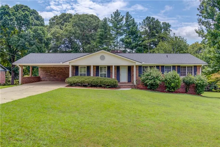Ranch-style residence featuring a brick facade, covered carport, and a prominent front lawn