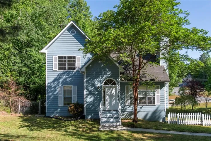 Charming two-story home featuring light blue horizontal siding, a peaked roofline with gable detailing, and a covered front entrance