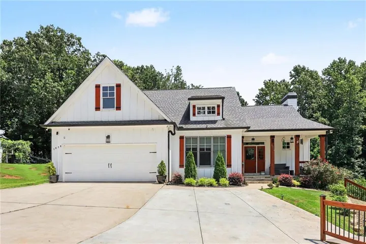 White board and batten siding, dark shingle roof, two-car garage, covered entry with wood columns, and red accent shutters