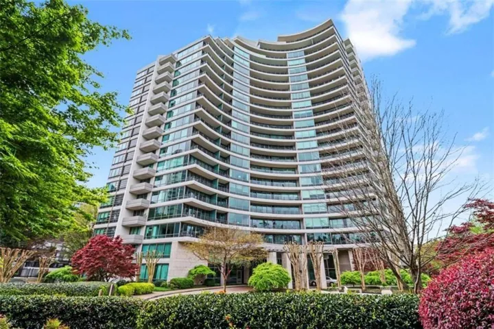 Curved architectural facade featuring extensive glazing, private balconies, and a manicured landscape with mature trees and shrubs