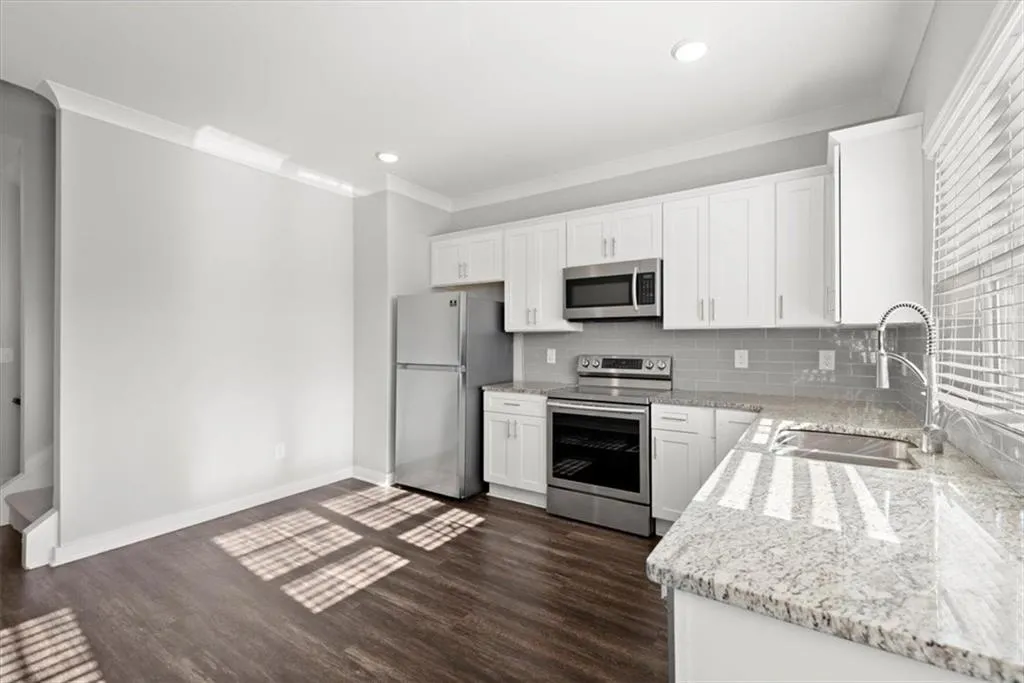 Kitchen featuring white cabinets, stainless steel appliances, light stone countertops, ornamental molding, and recessed lighting