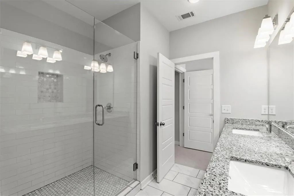 Bathroom with a shower stall, double vanity, and light tile patterned floors