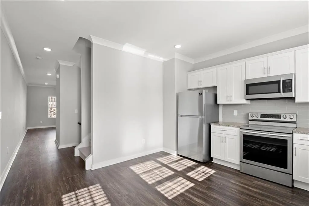 Kitchen featuring appliances with stainless steel finishes, white cabinets, decorative backsplash, dark wood finished floors, and ornamental molding