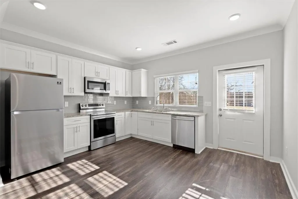 Kitchen featuring stainless steel appliances, white cabinets, backsplash, dark wood-style floors, and ornamental molding