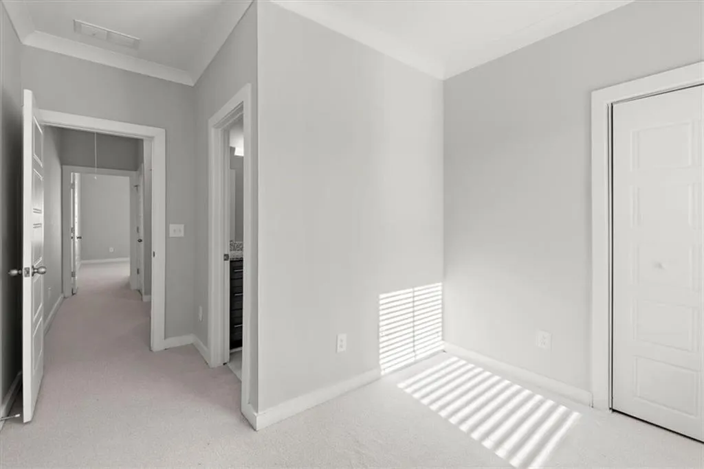 Unfurnished bedroom with light colored carpet, ornamental molding, and attic access