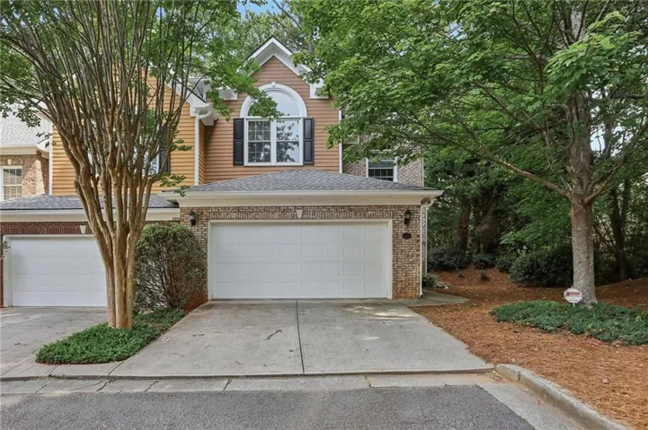Two-story property featuring a brick and siding exterior, arched window detail, two attached garages, and a concrete driveway