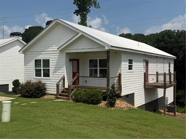 White siding exterior featuring a red entry door, white metal roof, front porch with wood columns and railings, and an elevated side deck