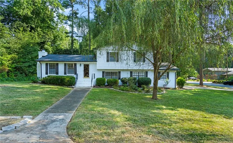 White two-story residence with dark shutters, a front entry path, and a mature weeping willow tree