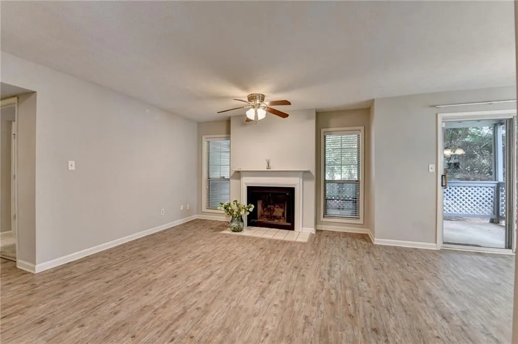 Unfurnished living room featuring a ceiling fan, wood finished floors, and a fireplace with flush hearth