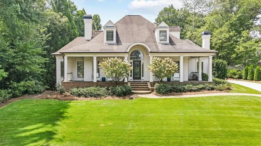 French Colonial residence featuring a symmetrical facade with cream-colored exterior walls, a distinctive mansard roof with dormers, and multiple chimneys
