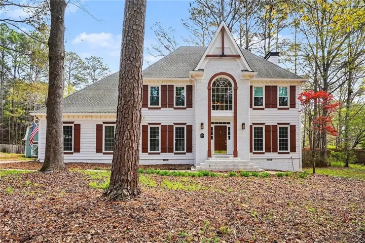 Two-story residence featuring white painted brick, a prominent arched window, dark wood shutters, and a covered entry