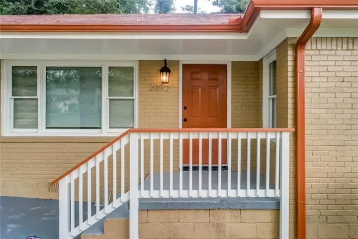 Brick exterior featuring a front entry door, covered porch, and white window frames