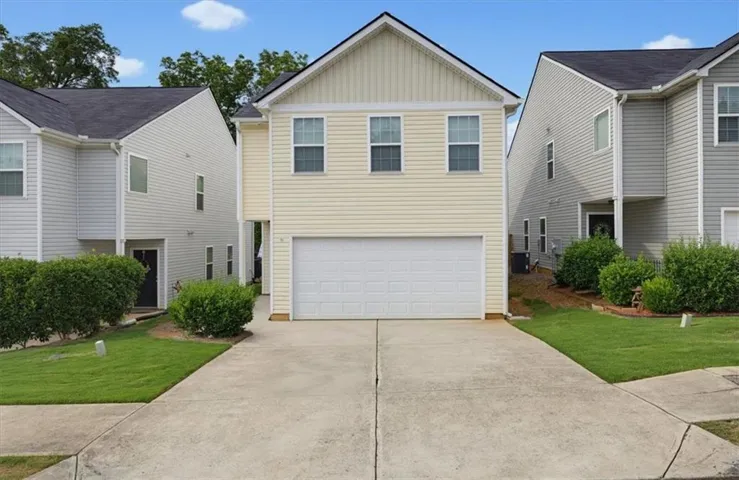 Two-story residence featuring light-colored siding, a prominent two-car garage, and a concrete driveway