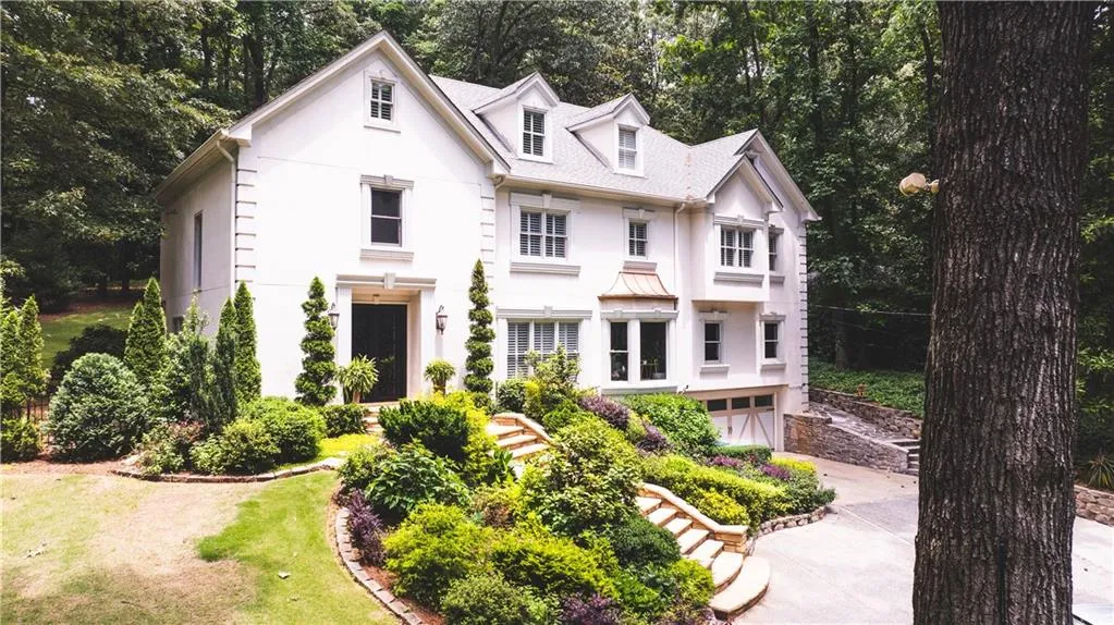View of front facade with stucco siding, concrete driveway, a garage, and view of wooded area