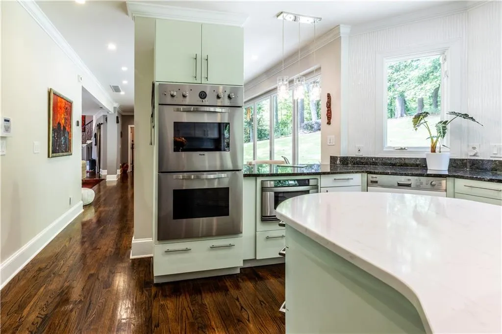Kitchen with stainless steel double oven, dishwashing machine, crown molding, dark wood-style flooring, and dark stone counters