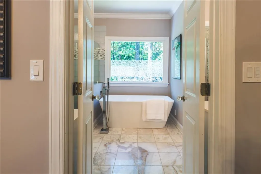 Bathroom with a freestanding bath, crown molding, and marble look tiles