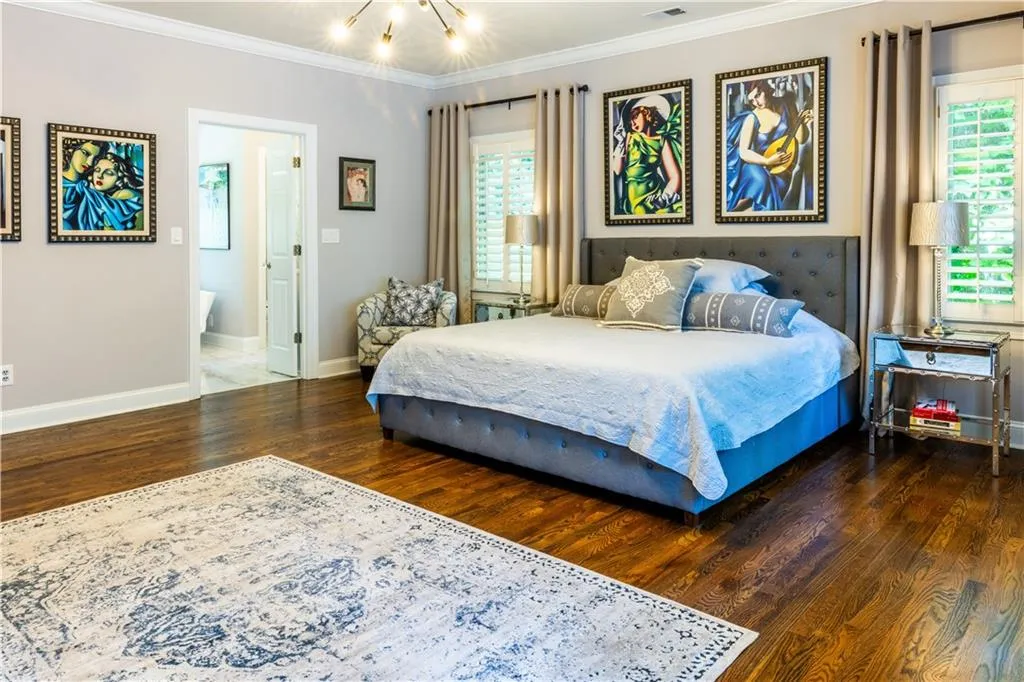 Bedroom with wood finished floors, ornamental molding, multiple windows, baseboards, and ensuite bath