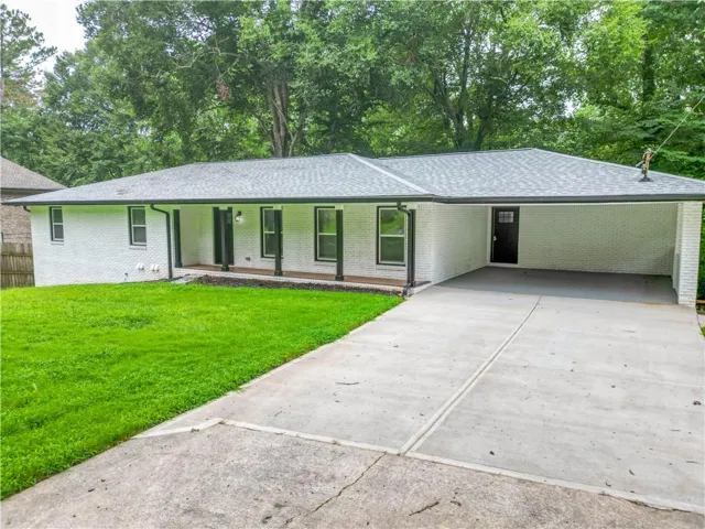 White painted brick exterior, dark asphalt shingle roof, covered carport, concrete driveway, and covered front porch