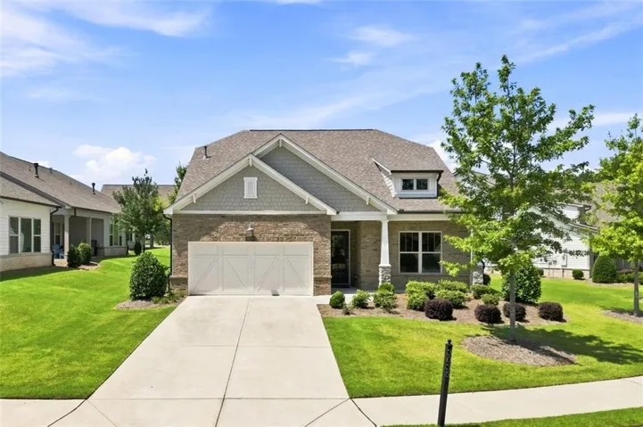 Brick and shingle exterior with a dormer window, an attached two-car garage, an elongated concrete driveway, and a front porch with a column accent