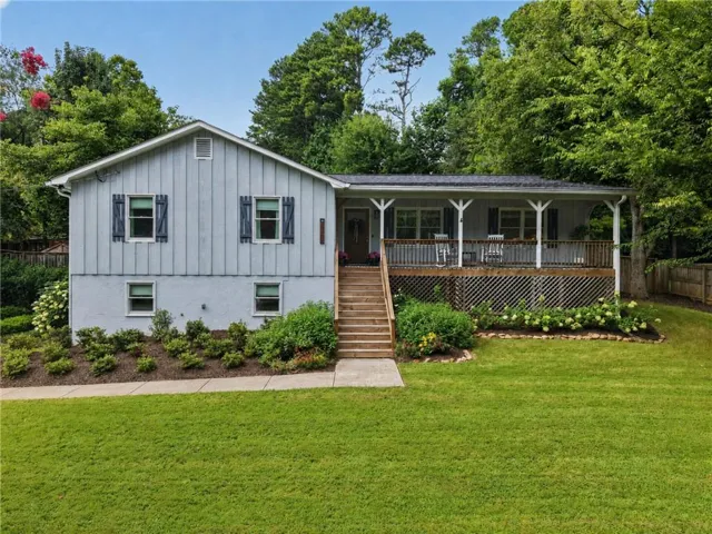 Split-level residence featuring a covered front porch, wood stairs, a manicured lawn, established landscaping, and a slatted privacy fence