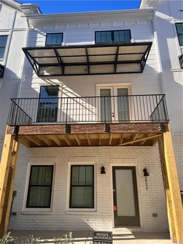 White brick facade with black-framed windows and a second-story wood-finish balcony featuring metal railings and a structural awning