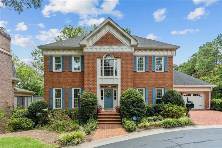 Charming brick Colonial featuring a symmetrical facade with a centered entry portico, multi-pane windows with blue shutters, and a peaked gable roofline