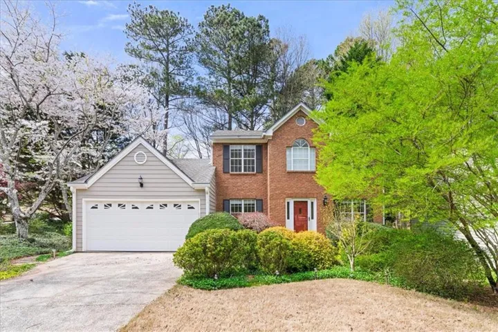 Brick and siding exterior with an attached garage, featuring a red entry door, an arched window, and mature landscaping