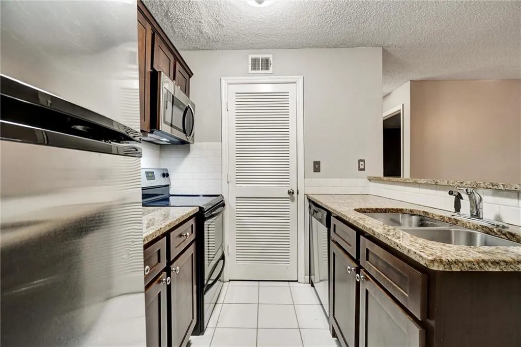 Kitchen with stainless steel appliances, light stone counters, dark brown cabinetry, light tile patterned floors, and a textured ceiling