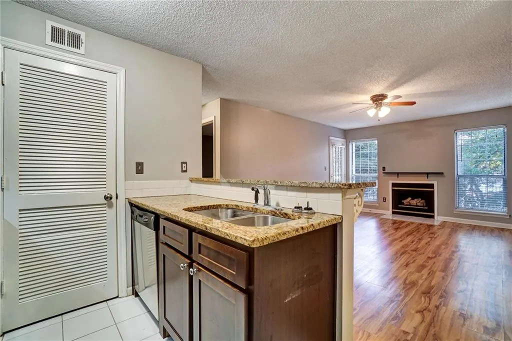 Kitchen with a peninsula, dark brown cabinetry, a textured ceiling, light stone counters, and a fireplace with flush hearth