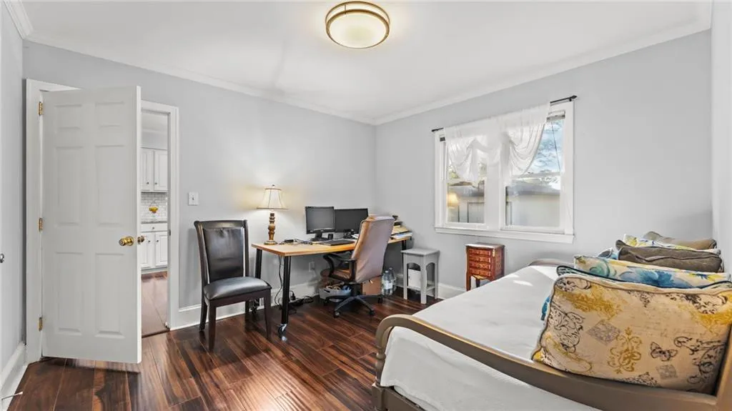 Bedroom with ornamental molding, dark wood-type flooring, and an office area