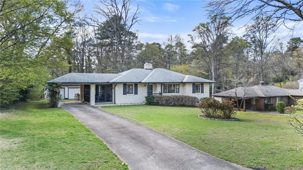 Ranch-style house featuring an attached carport, a front lawn, asphalt driveway, a chimney, and view of scattered trees