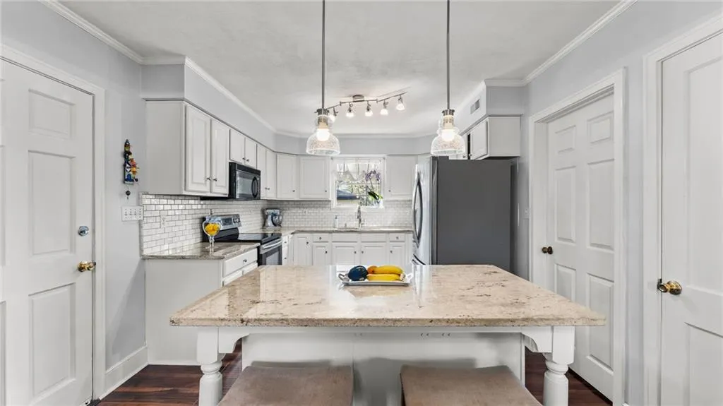 Kitchen featuring light stone countertops, white cabinetry, stainless steel appliances, dark wood-type flooring, and crown molding
