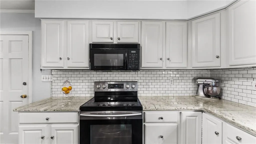 Kitchen with stainless steel electric stove, white cabinets, black microwave, light stone countertops, and crown molding