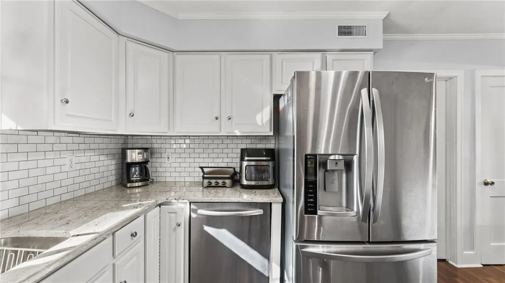 Kitchen featuring stainless steel appliances, light stone counters, white cabinets, crown molding, and decorative backsplash