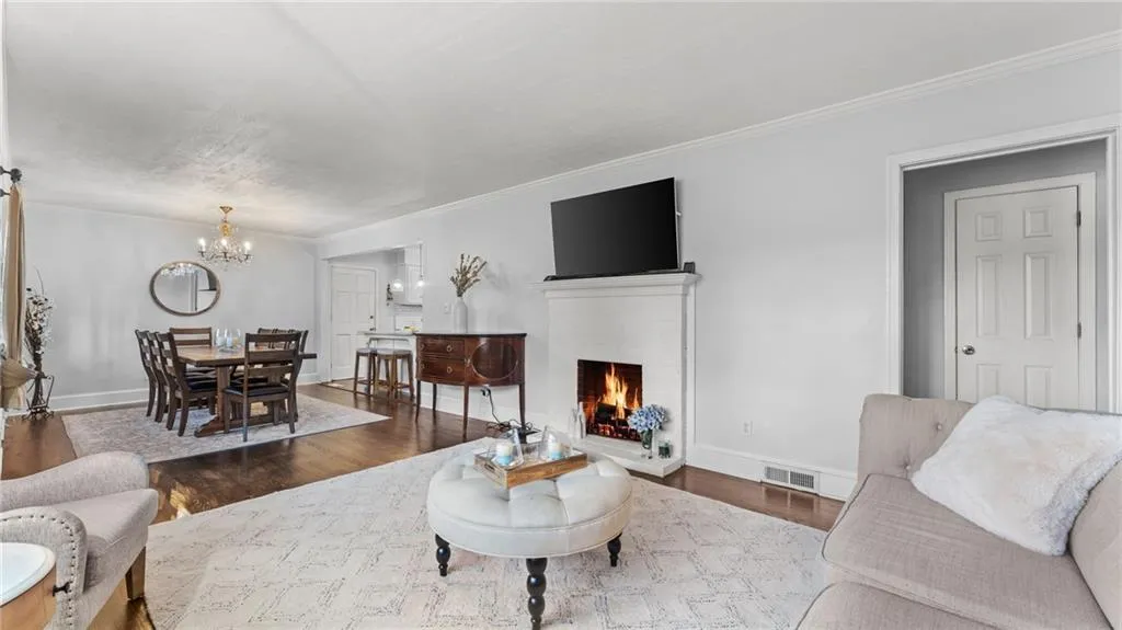 Living room featuring wood finished floors, a brick fireplace, suspended lighting, and crown molding