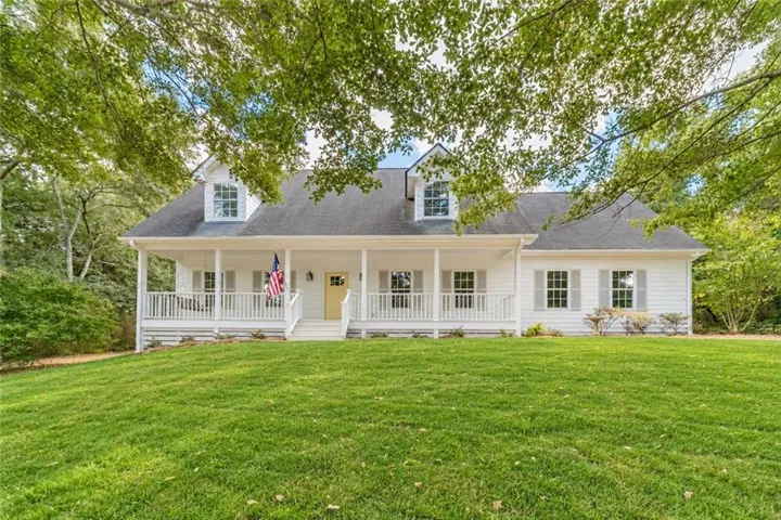 White facade featuring a covered front porch, dormer windows, and a yellow entry door