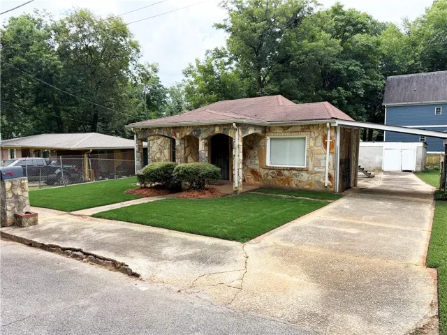 Stone veneer exterior with an integrated carport, established landscaping, and a concrete driveway