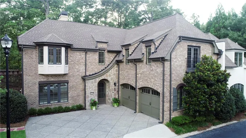 Brick and stone exterior featuring a bay window, arched entry, two-car garage with arched doors, and a decorative balcony