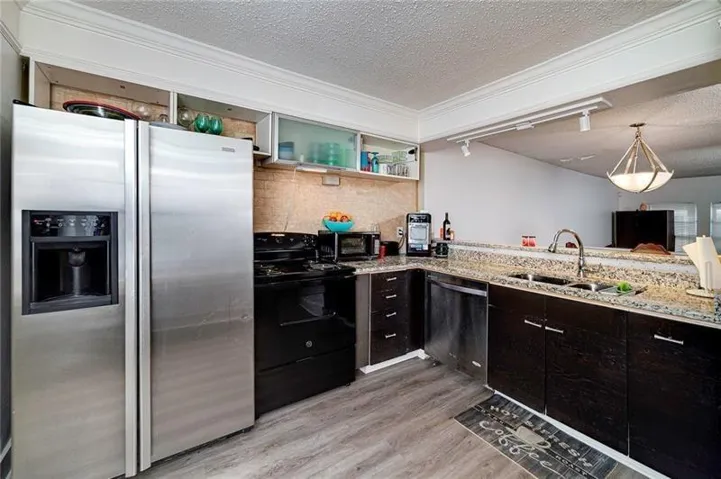 Kitchen featuring granite countertops, wood-finish flooring, stainless steel appliances, dark cabinetry, and track lighting