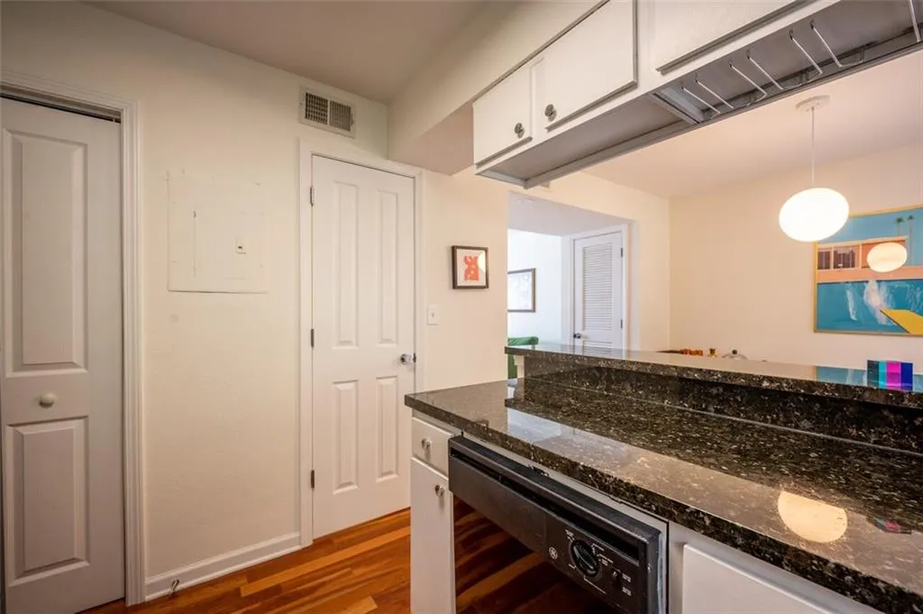 Kitchen featuring white cabinetry, wood finished floors, wine cooler, hanging light fixtures, and dark stone countertops