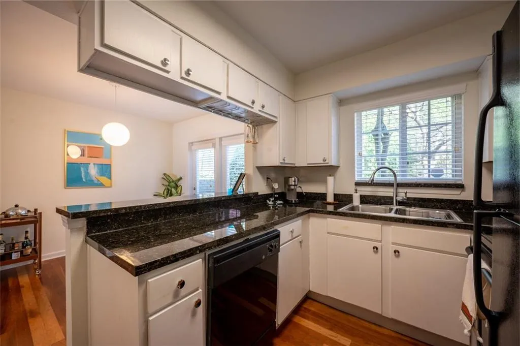 Kitchen with a peninsula, black appliances, white cabinetry, dark wood-style flooring, and dark stone countertops