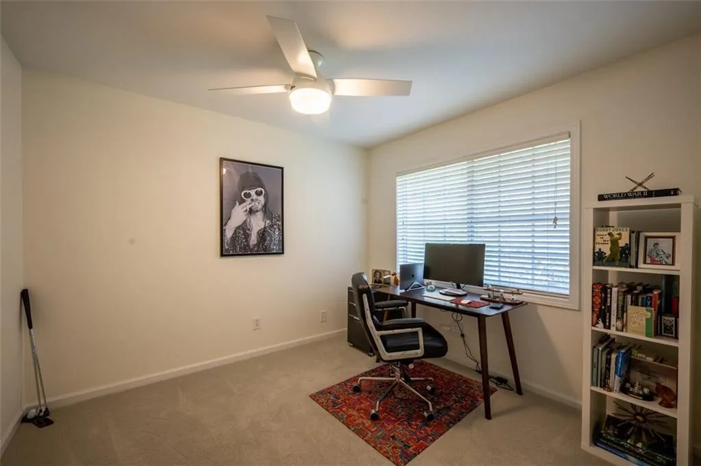 Carpeted home office featuring ceiling fan and baseboards