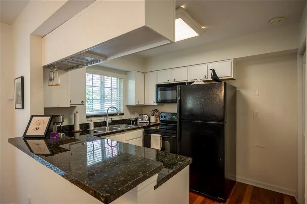 Kitchen with black appliances, a peninsula, dark wood-type flooring, white cabinetry, and dark stone counters