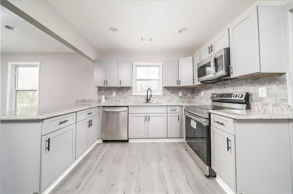 Kitchen featuring a sink, tasteful backsplash, appliances with stainless steel finishes, a peninsula, and light wood-type flooring