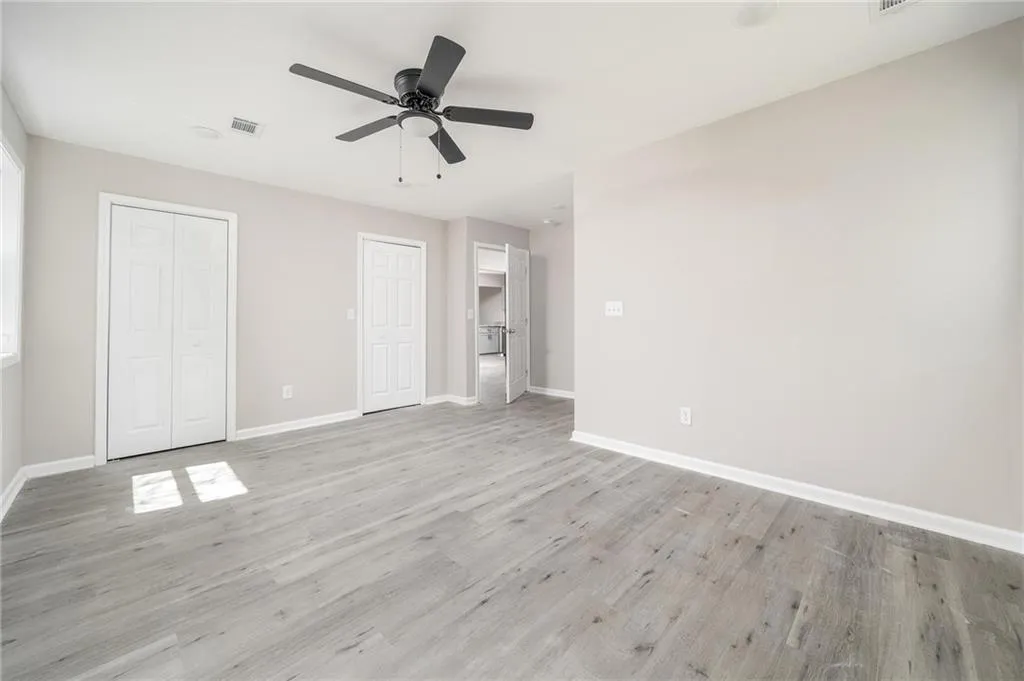 Unfurnished bedroom with baseboards, a ceiling fan, two closets, and light wood-style floors