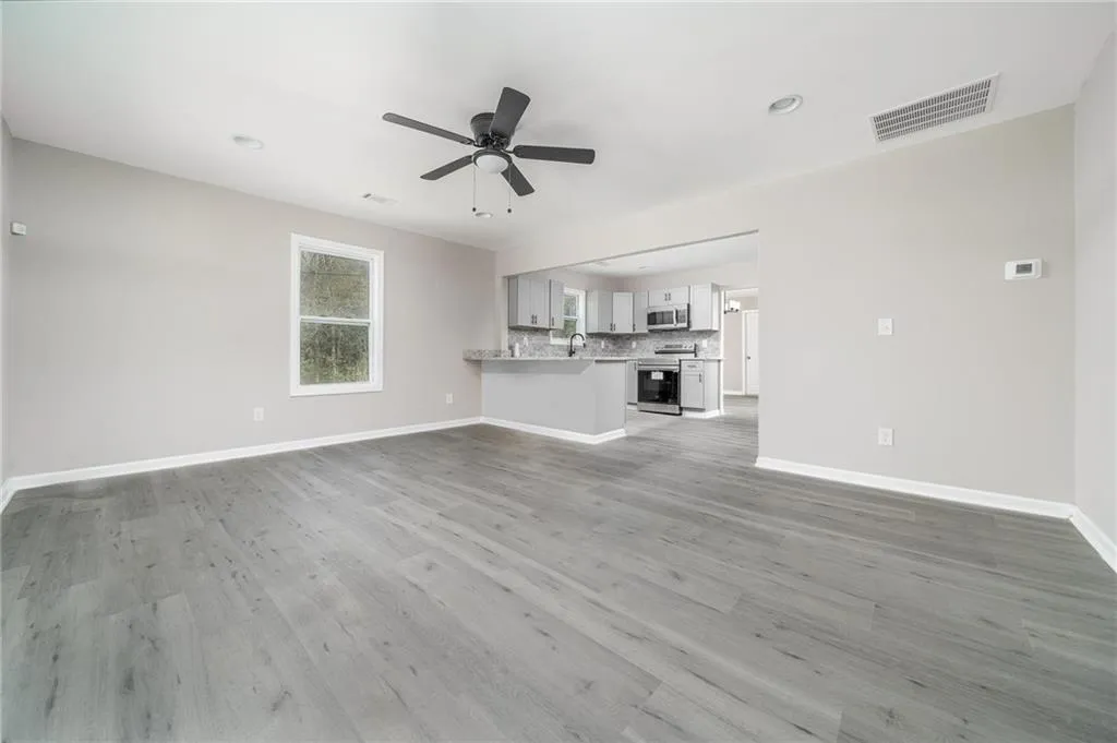 Unfurnished living room with visible vents, light wood finished floors, baseboards, ceiling fan, and a sink