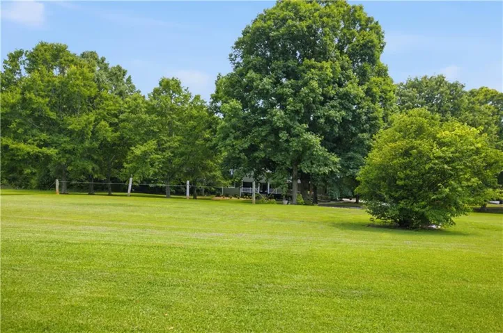 Expansive grassy area with mature trees and a partial fence line