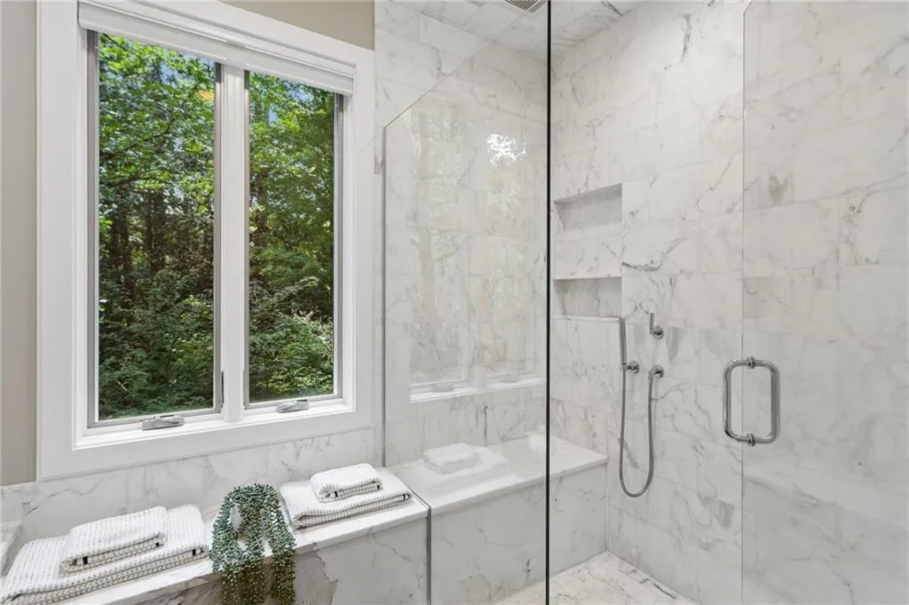 Glass-enclosed shower with wall-mounted fixtures, built-in shelving, and a shower bench